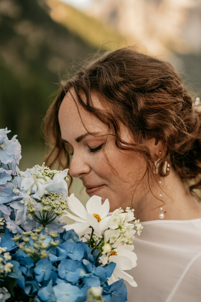 Woman smelling blue and white flowers outdoors.
