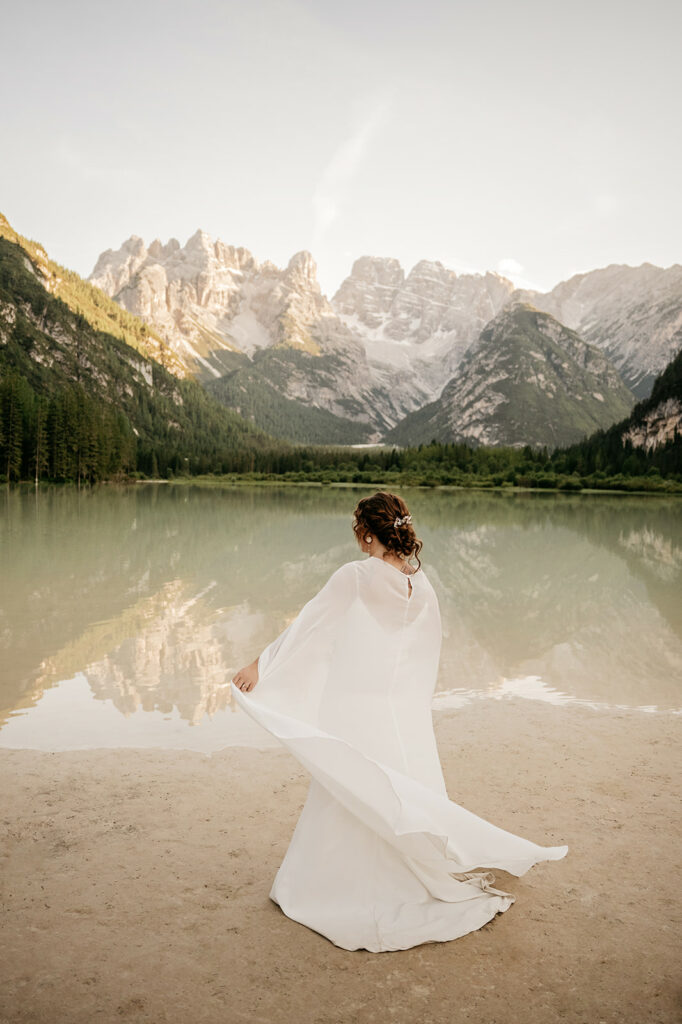 Bride standing by mountain lake, scenic view.