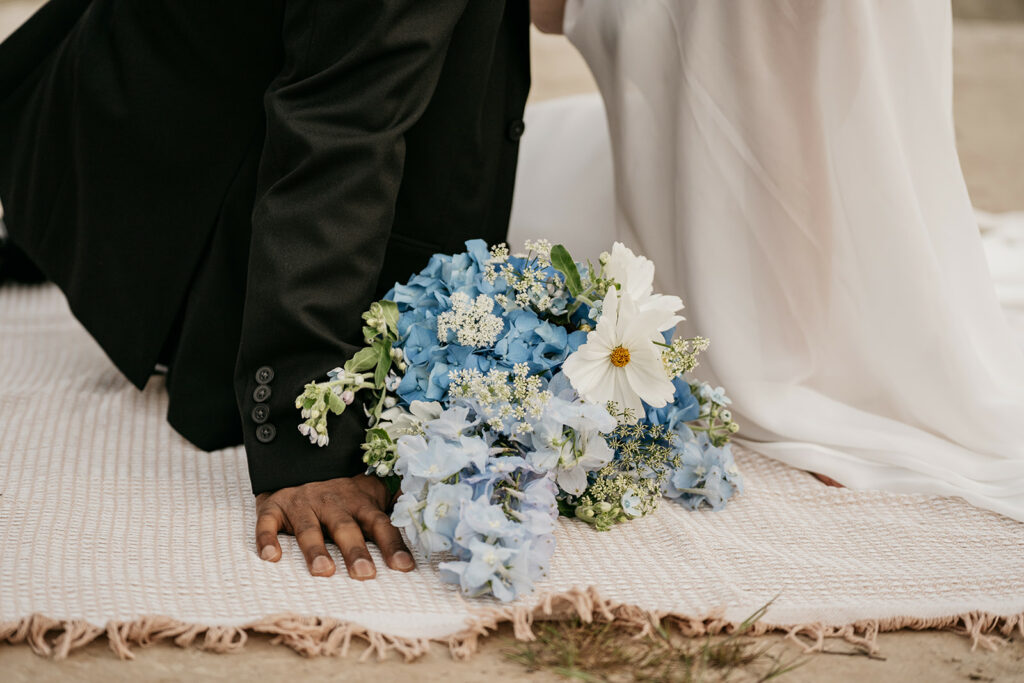 Couple kneeling with blue and white bouquet.