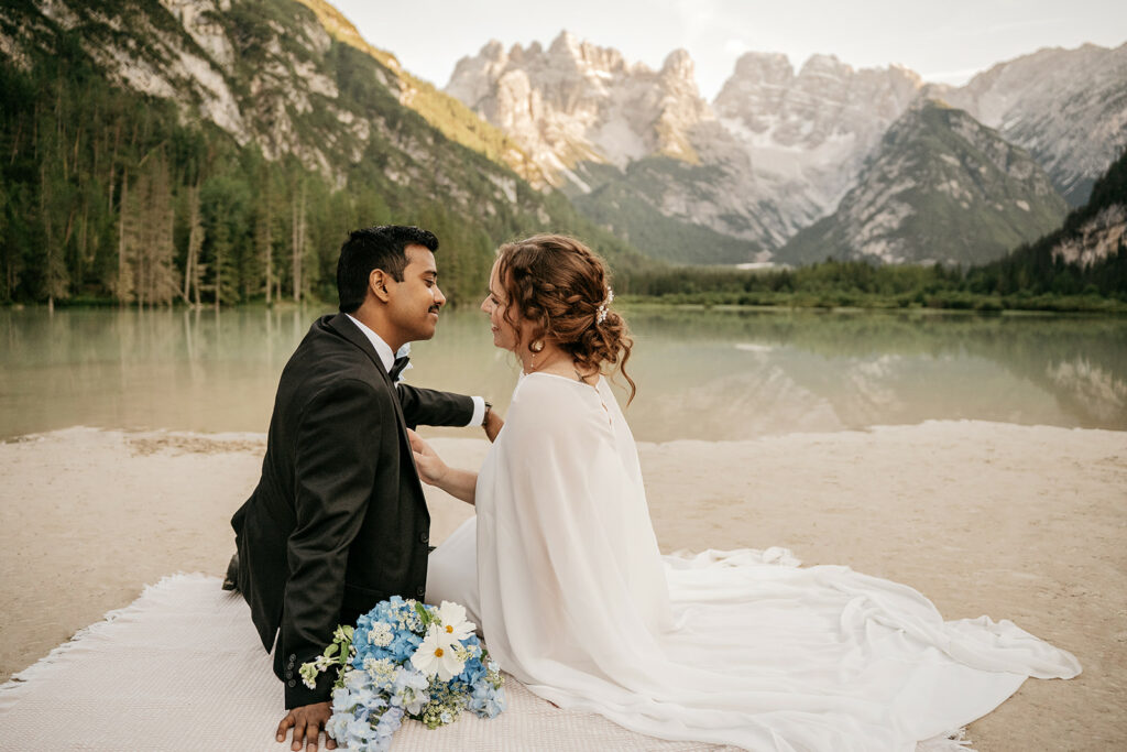 Couple sitting by mountain lake with bouquet.
