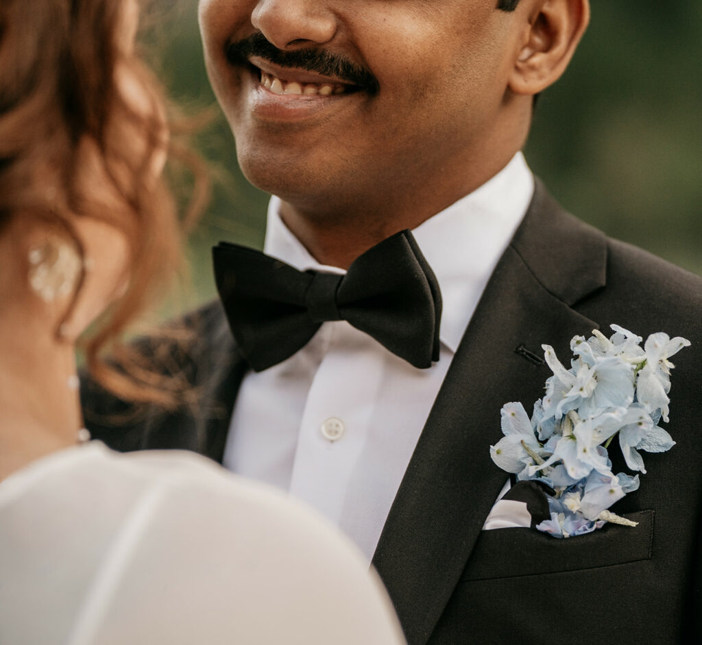 Groom smiling, wearing black suit and bowtie.
