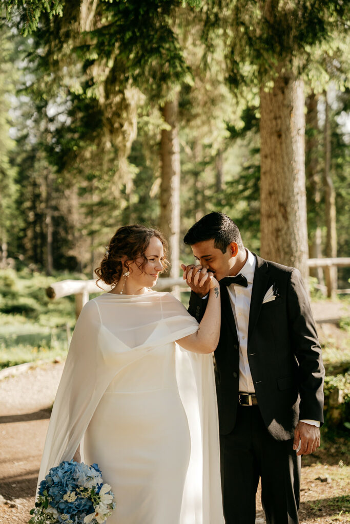 Bride and groom kissing hands in forest setting.