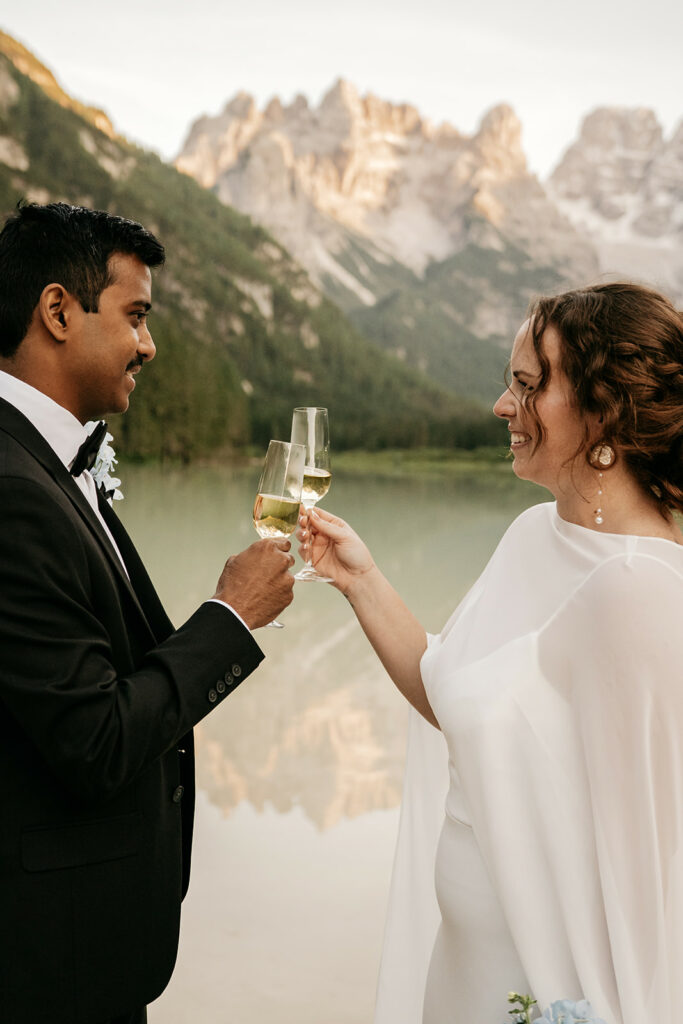 Wedding couple toasting by mountain lake.