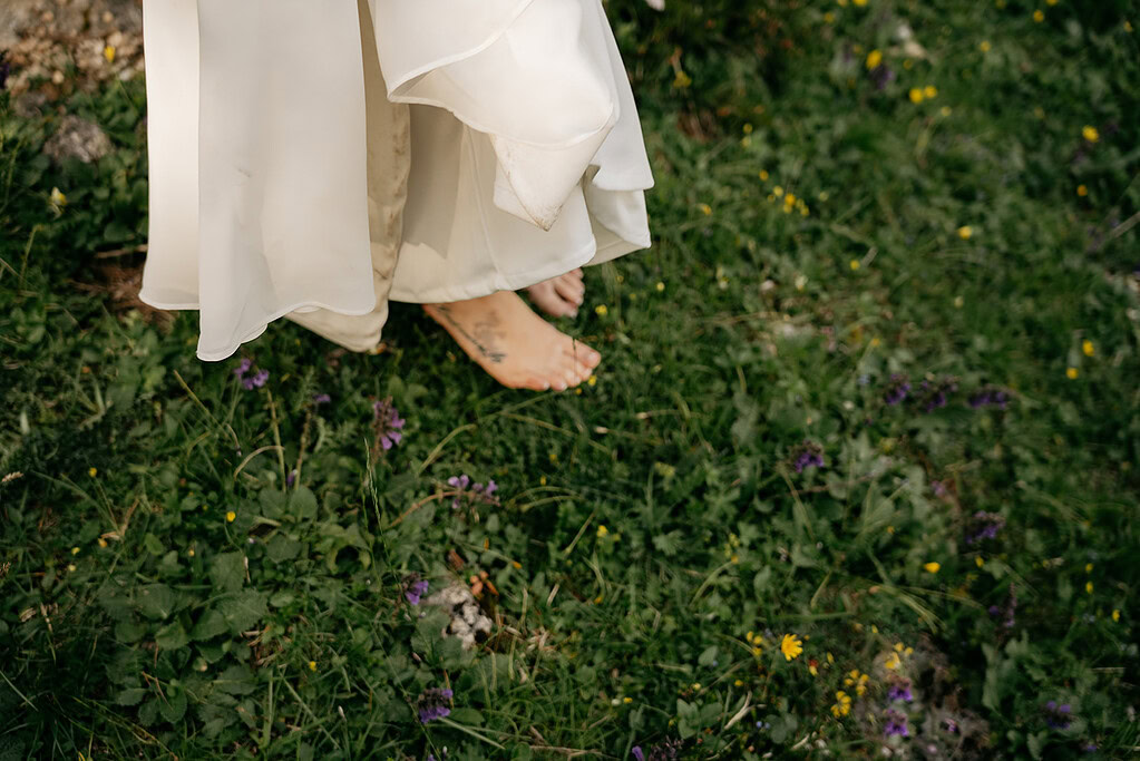 Barefoot person in wedding dress on grassy field.