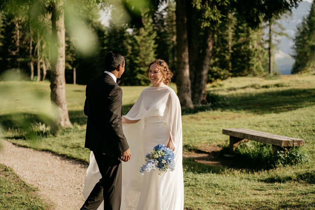 Bride and groom in forest, holding blue flowers.