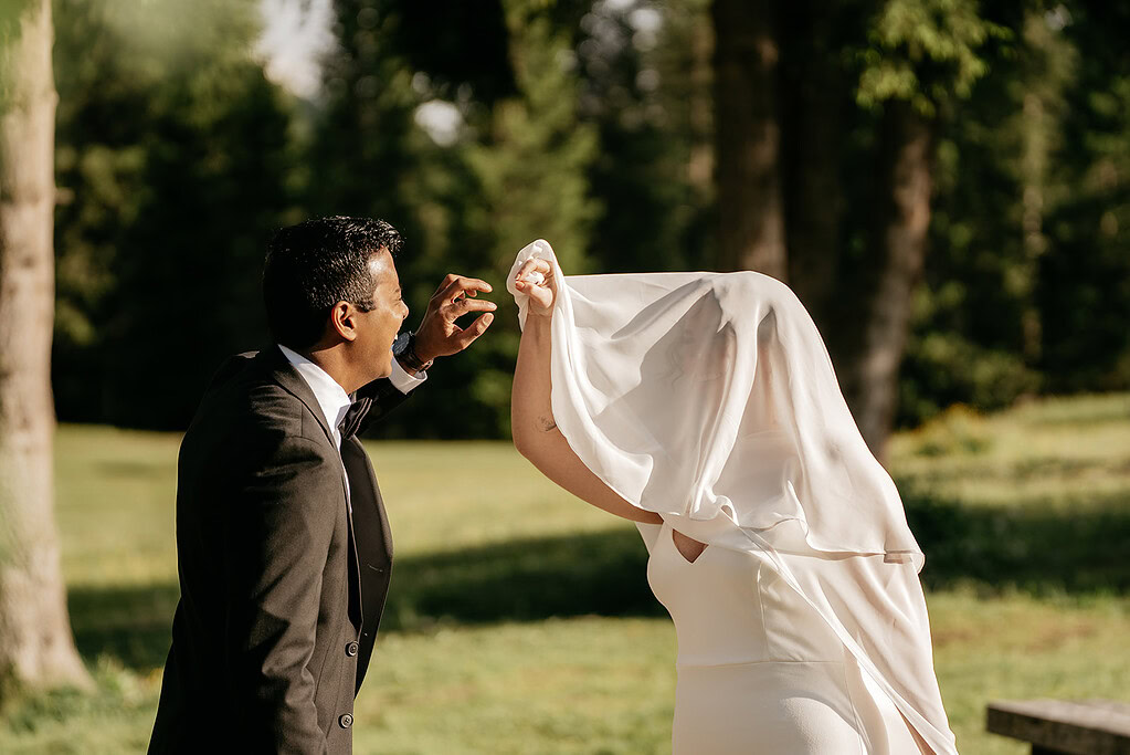 Groom lifting bride's veil outdoors.