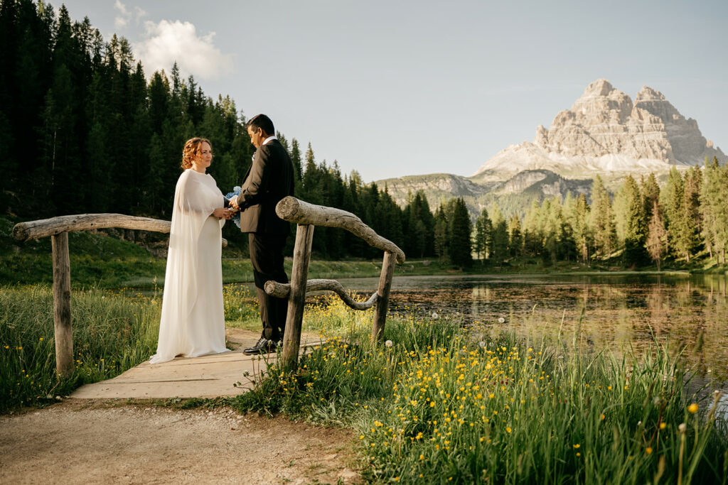 Couple holds hands on wooden bridge in mountains.