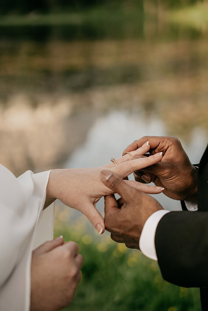 Couple exchanging rings by a lake.