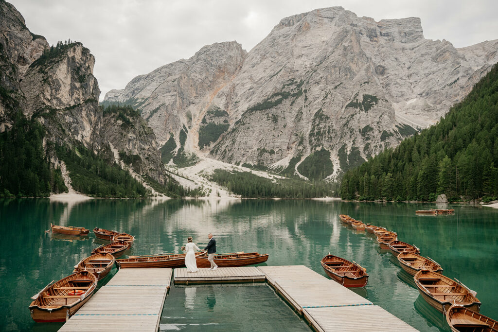 Couple on dock with boats, mountain lake scene.