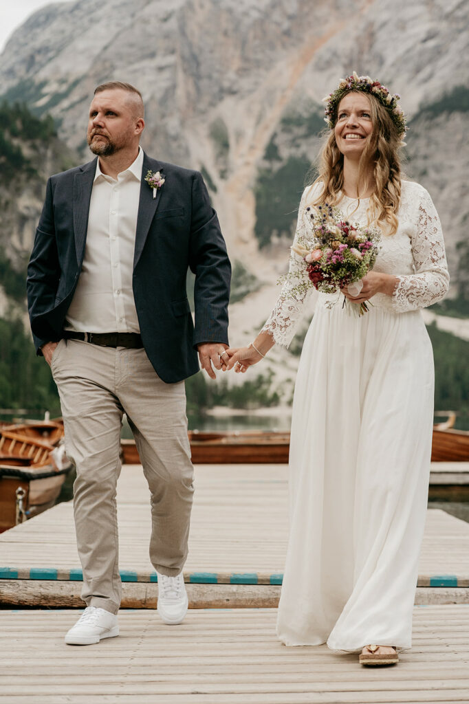 Couple holding hands on wooden dock, smiling.