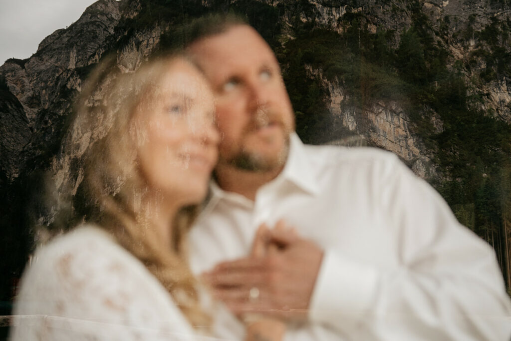 Couple embraces with mountain reflection backdrop.