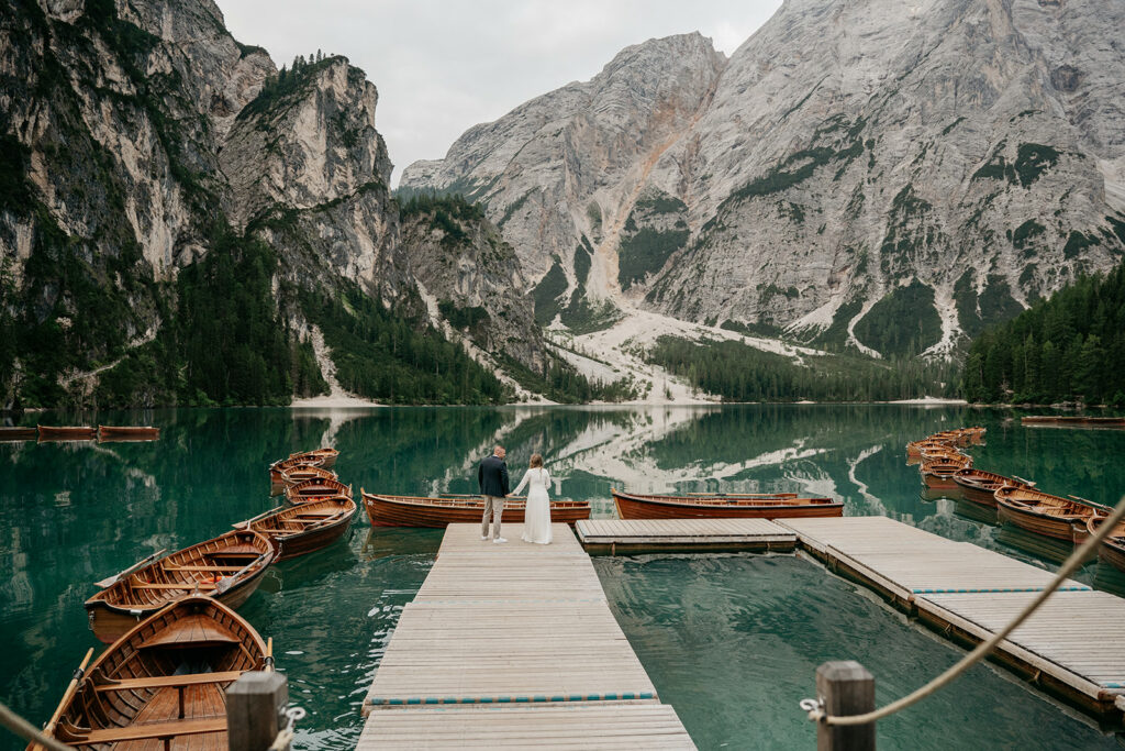 Couple on dock by mountain lake with boats.