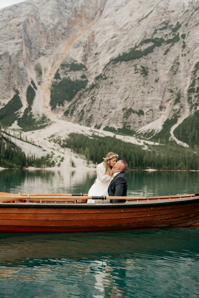 Bride and groom kissing on boat by mountain lake.