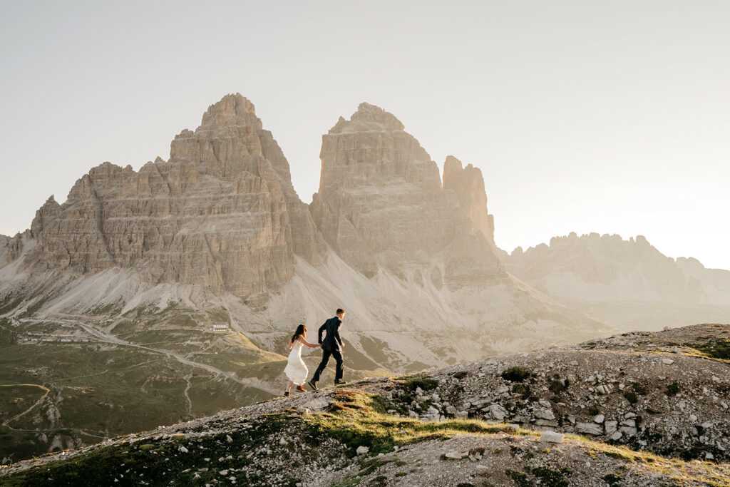 Couple hiking near mountain peaks at sunrise.