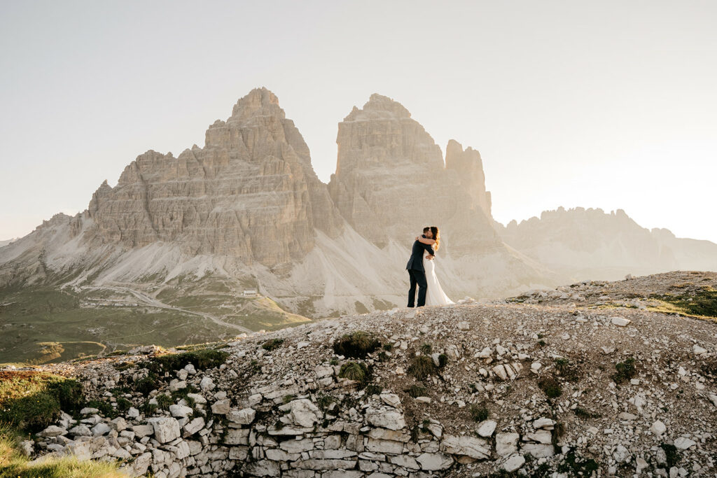 Couple embraces on mountain with stunning sunset backdrop.