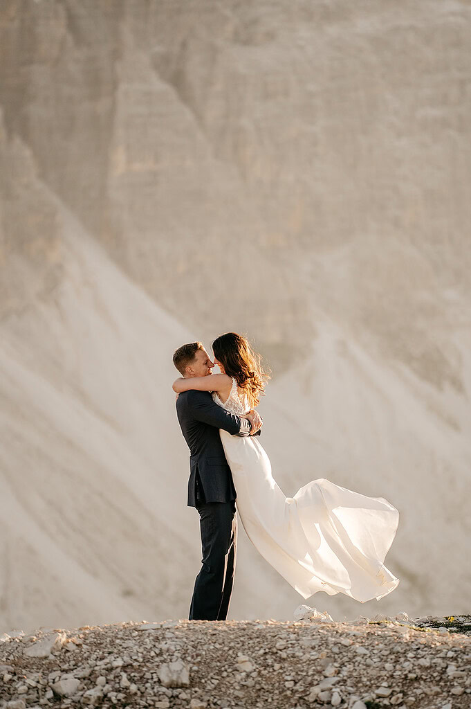 Couple embracing on rocky landscape in wedding attire.
