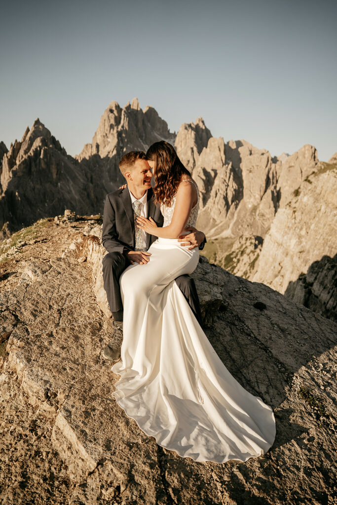 Bride and groom on mountain summit at sunset.