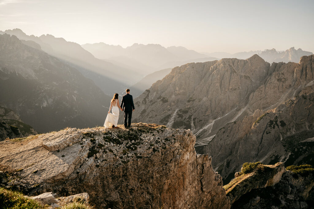 Couple standing on mountain cliff at sunset.