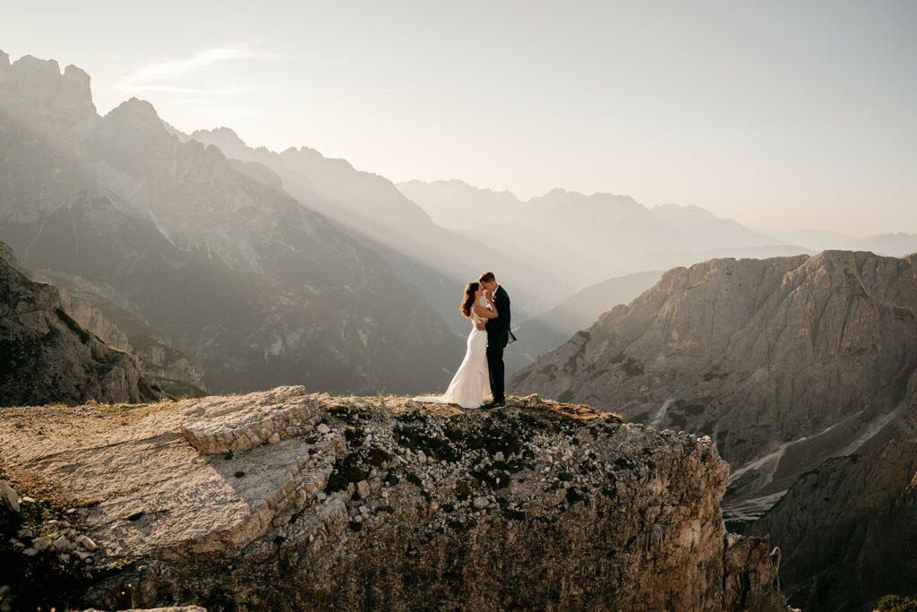 Couple embraces on mountain cliff during sunset.