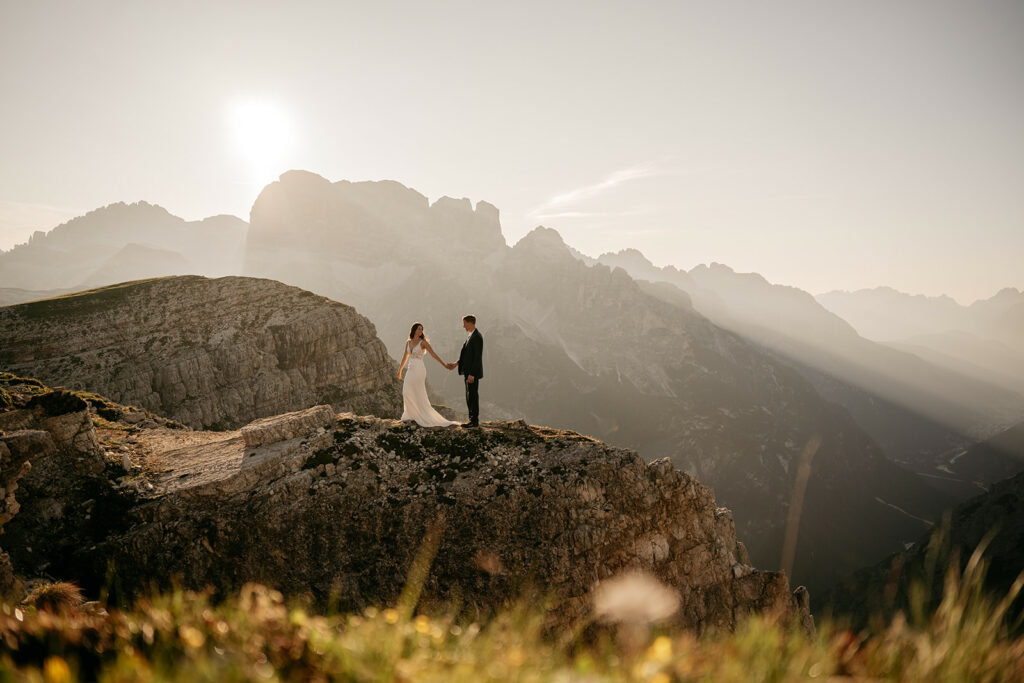Couple holding hands on mountain cliff at sunset.