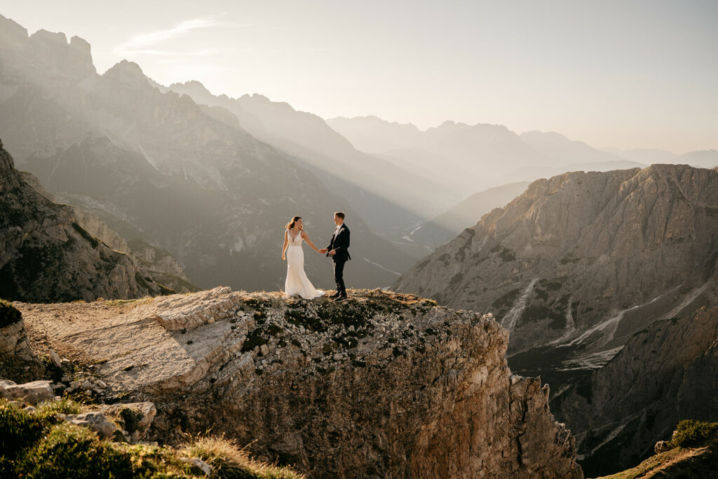 Couple holding hands on mountain cliff at sunset.