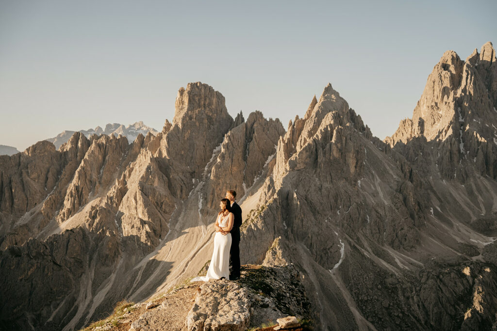 Couple embracing on mountain peak with rocky backdrop.