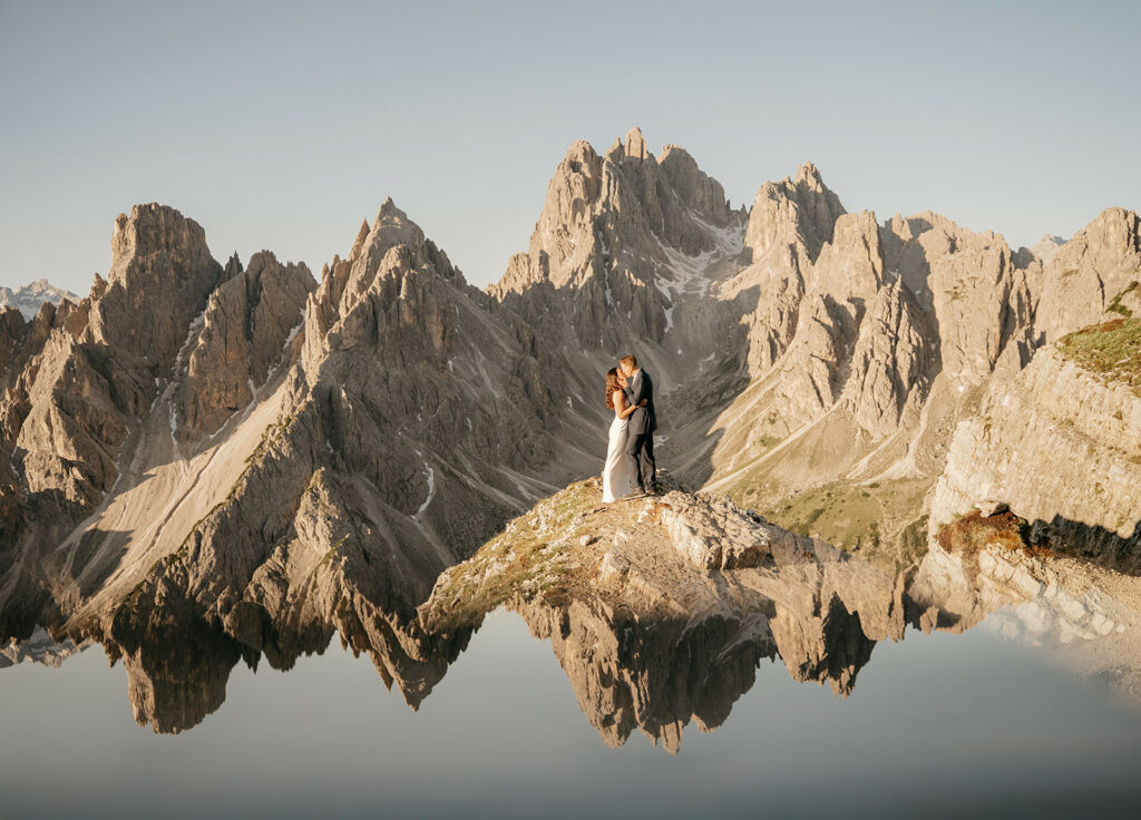 Couple embracing on mountain peak with reflection.