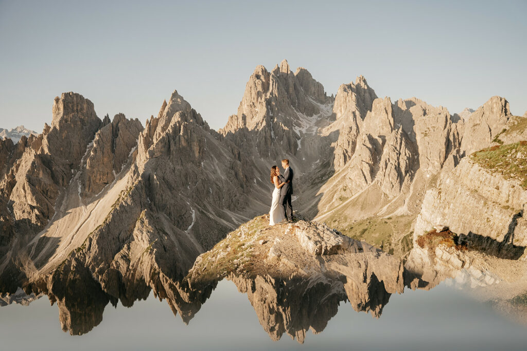 Couple stands on mountain peak with reflection