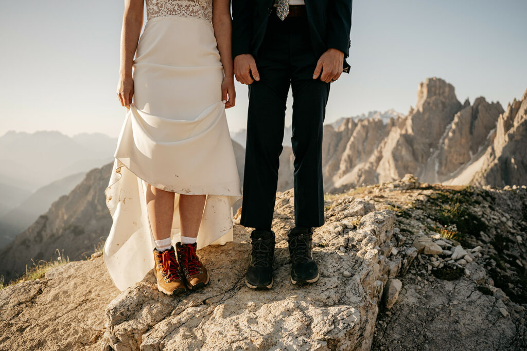 Couple in wedding attire and hiking boots on mountain.