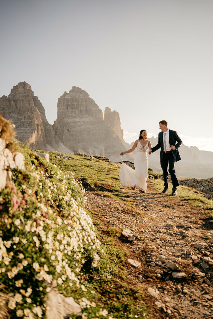 Couple hiking, wedding attire, mountain background, sunset.