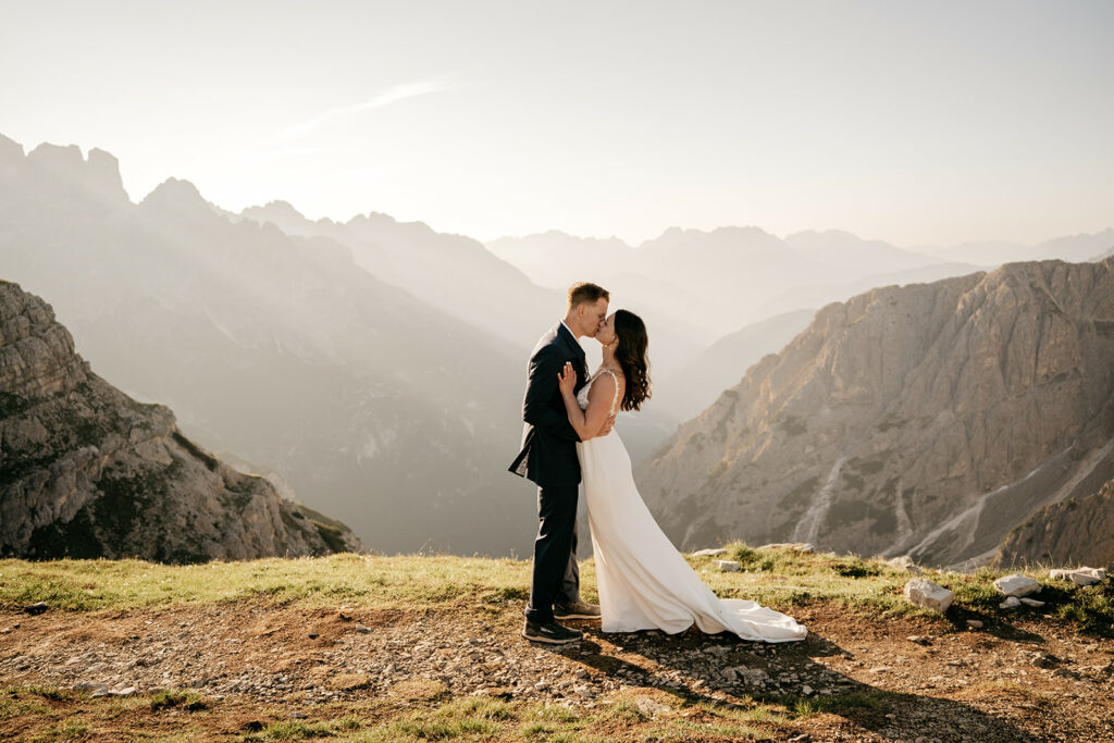 Bride and groom kissing on mountain at sunset.