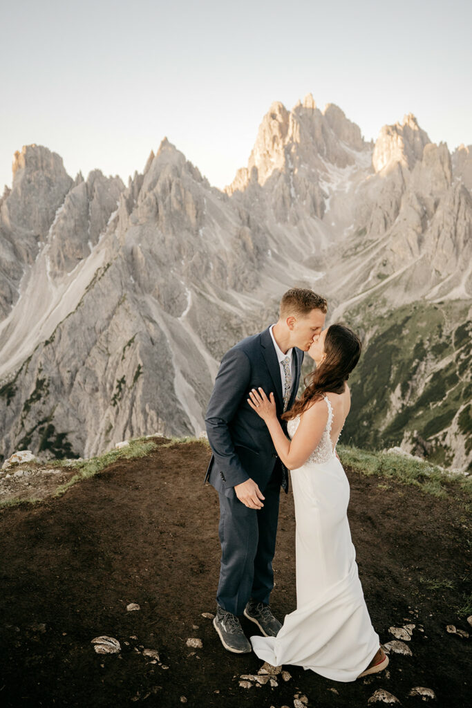 Couple kissing on mountain with rocky peaks background.
