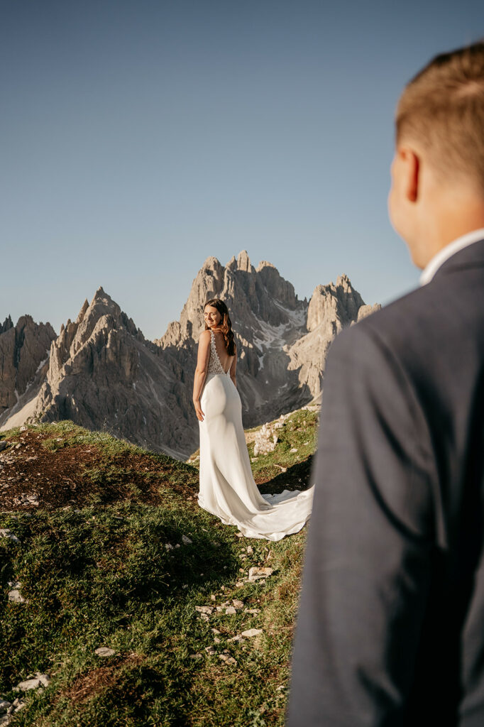 Bride in mountains, groom in foreground.