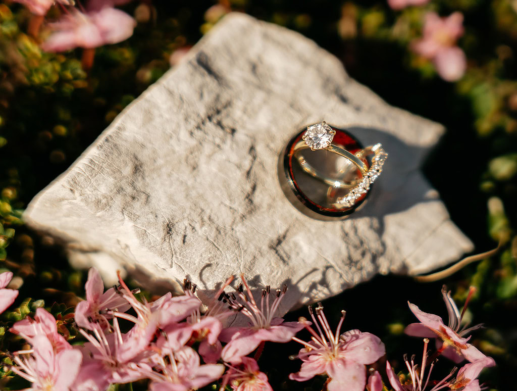 Wedding rings on stone with pink flowers.