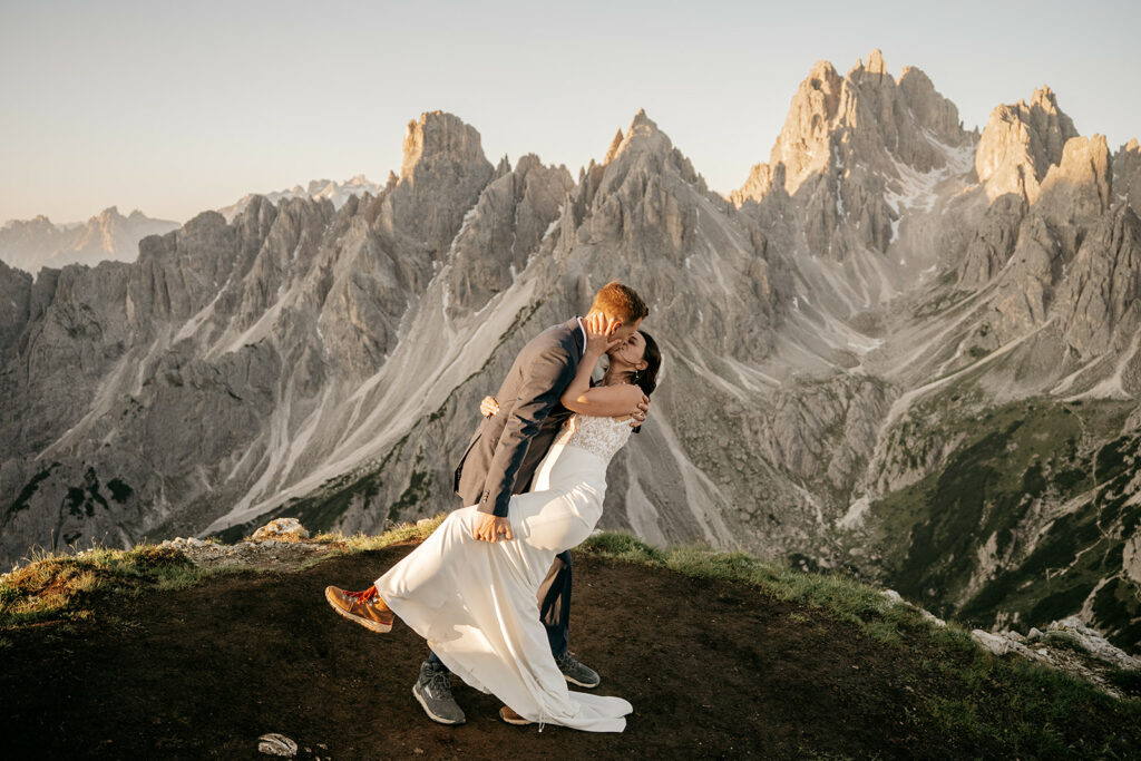 Couple kissing on mountain peak at sunset.