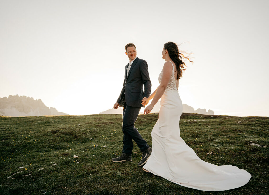 Couple holding hands on grassy hill at sunset.