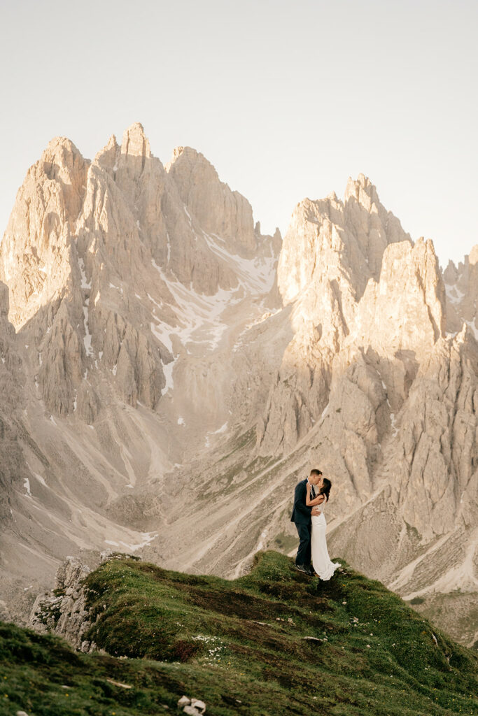 Couple embraces on mountain with scenic backdrop.