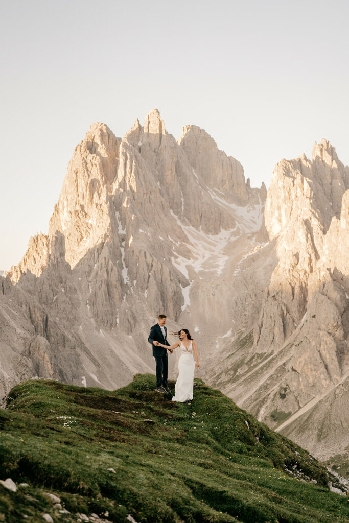 Couple standing on mountain landscape in wedding attire.