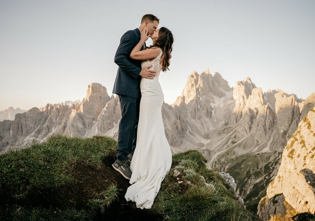 Couple kissing on mountain peak at sunset.