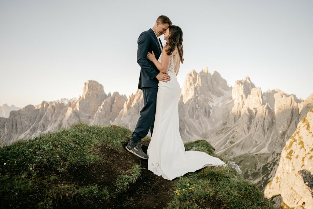 Bride and groom embrace on mountain edge.