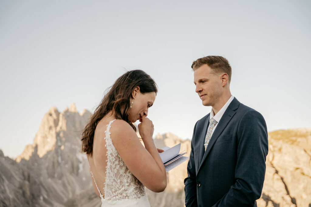 Bride reading vows to groom in mountain setting.