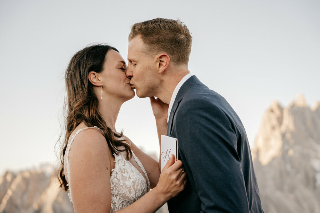 Bride and groom kissing in mountain setting.