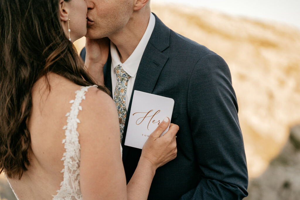 Bride and groom kissing, holding vow book.