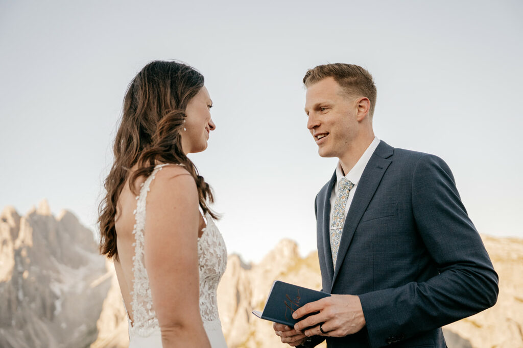 Couple exchanging vows outdoors, scenic mountain backdrop.