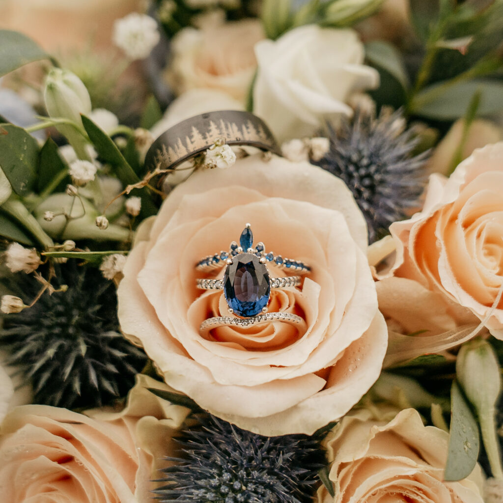 Blue gemstone ring on peach roses with greenery.