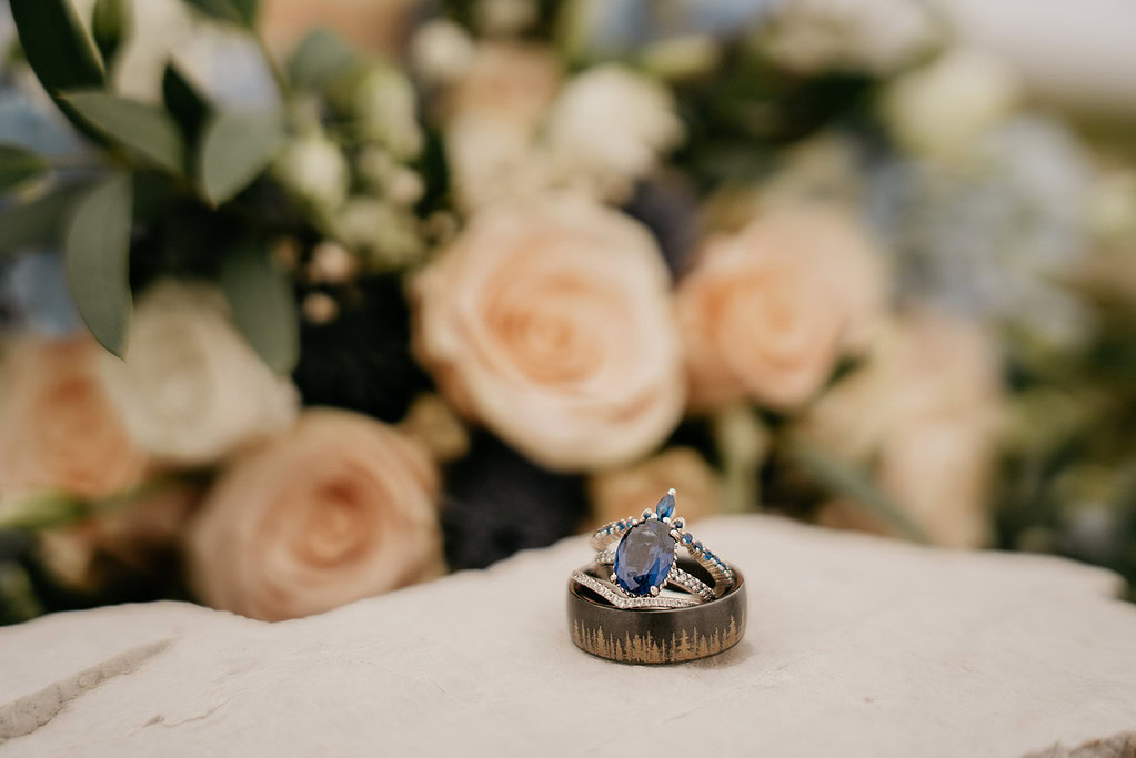 Wedding rings with blue gemstone, floral background.