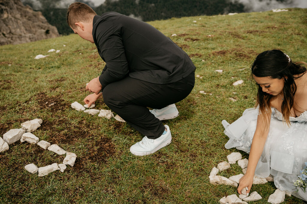 Couple arranging rocks on grassy hillside.
