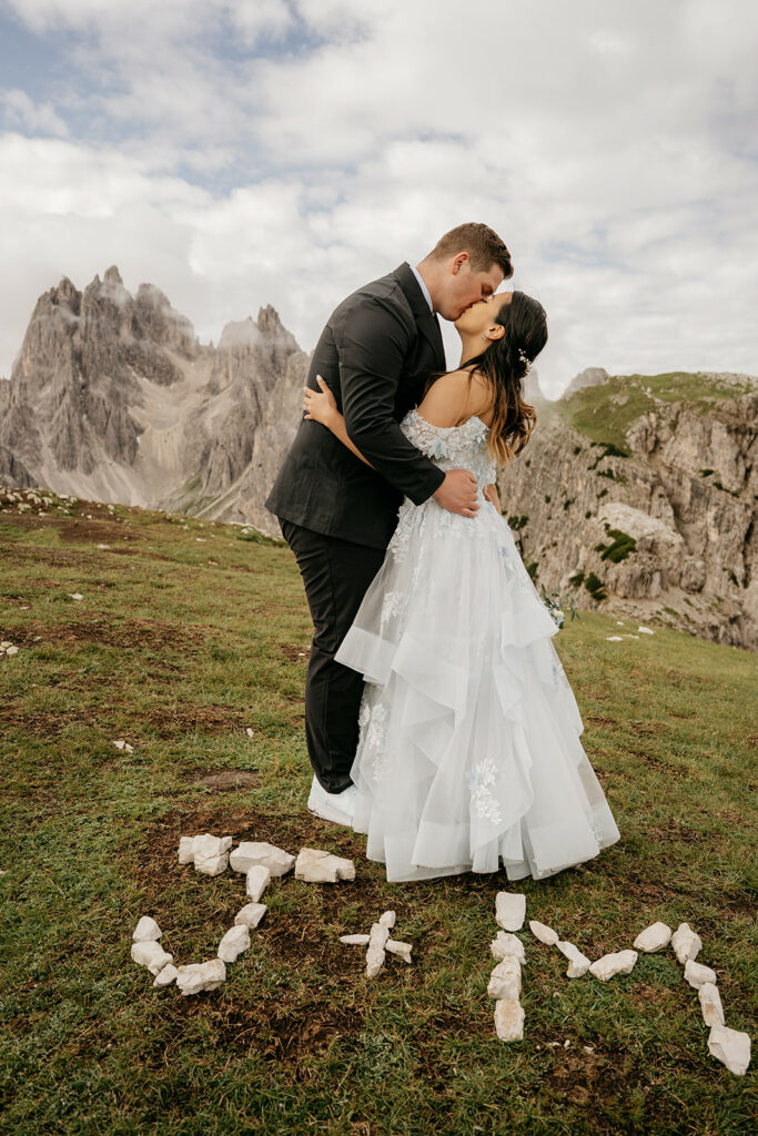 Couple kisses on mountain landscape with rock initials.