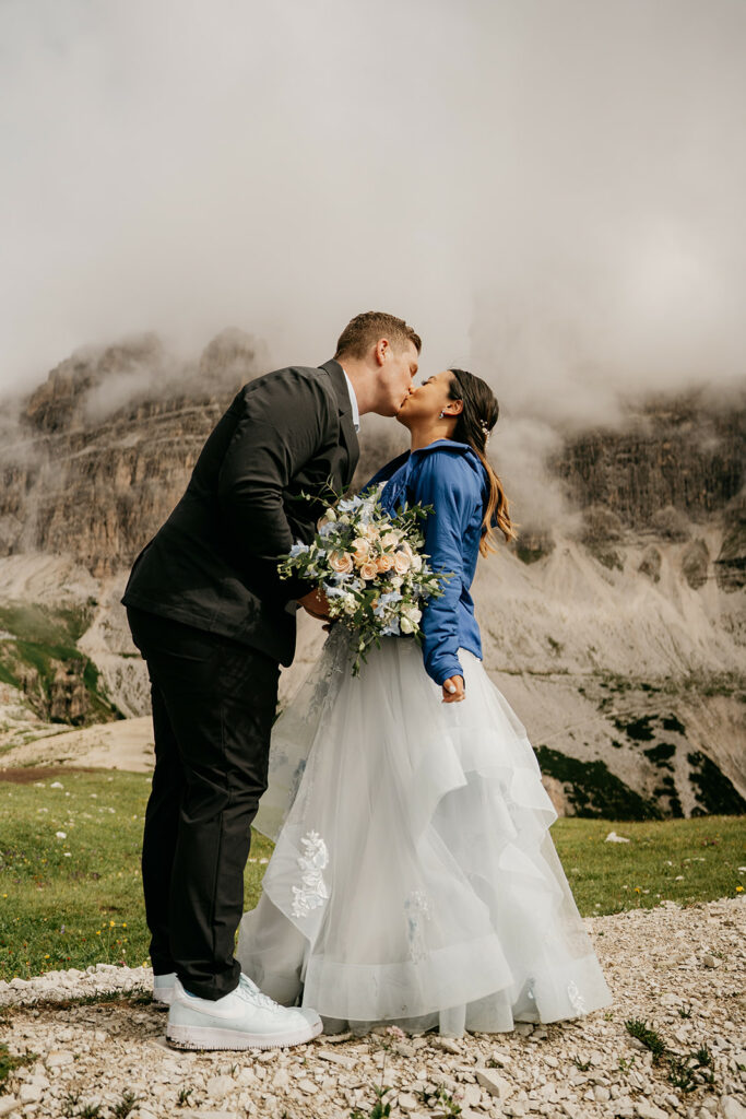 Couple kissing in mountains, wedding attire.