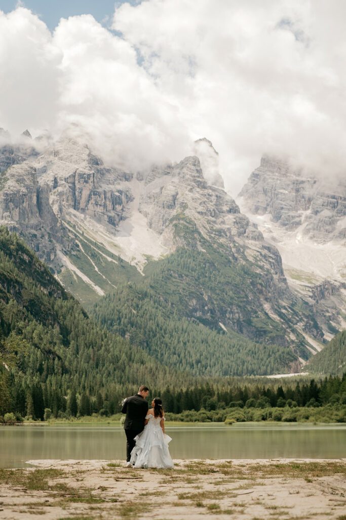 Couple walking by lake with mountain backdrop.
